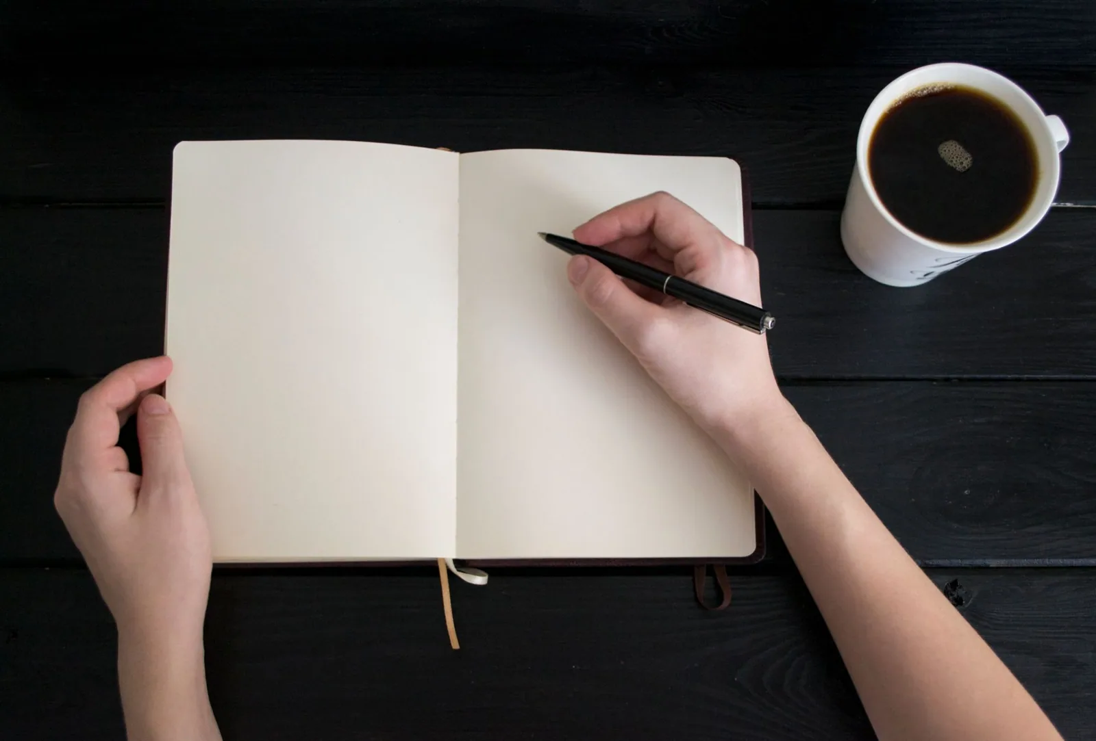 Open notebook, pen and coffee on a dark table