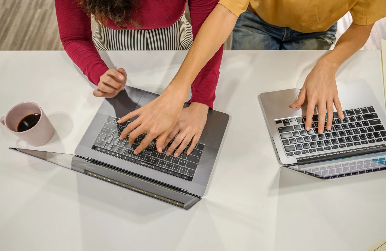 Two laptops and a coffee cup on a shared desk