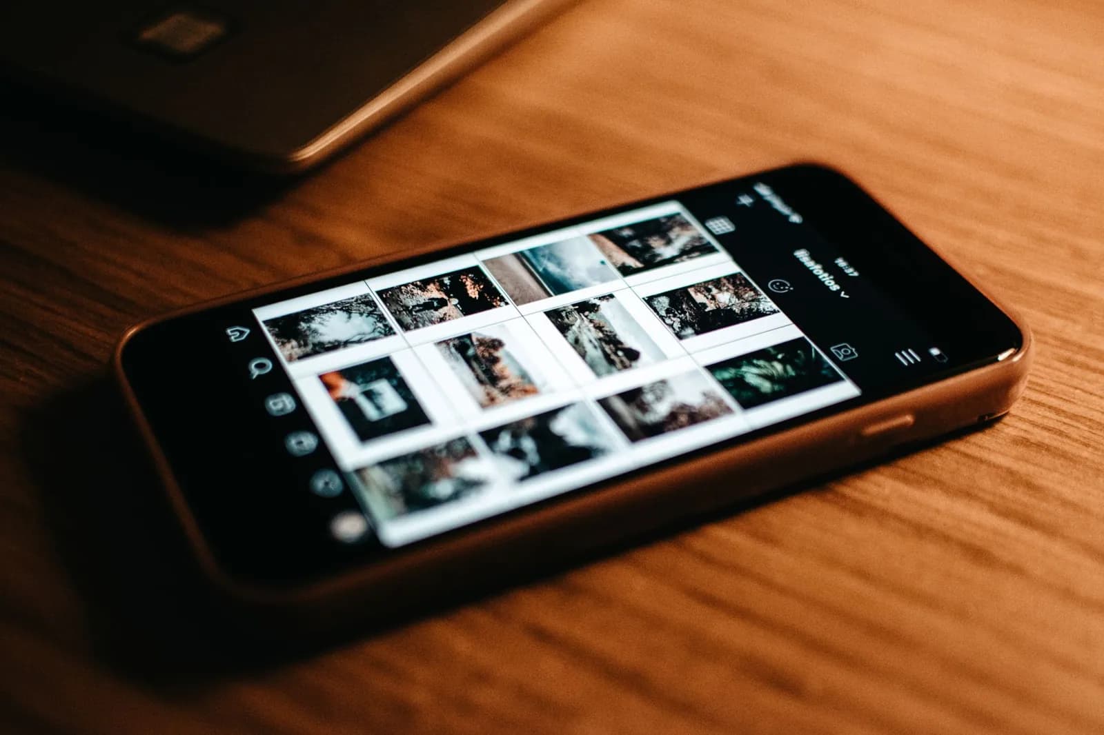 Phone showing a photo grid on a wooden desk
