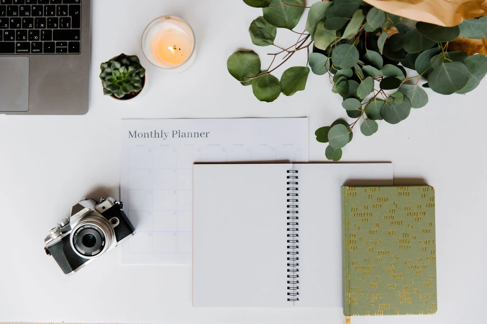 Monthly planner, notebook and camera on a white desk